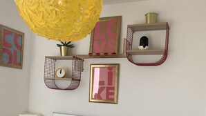 A bedroom with a bed, a nightstand, a lamp, a wall-mounted shelf with decorative items, and a hanging light fixture. - London Walthamstow Flat (London)