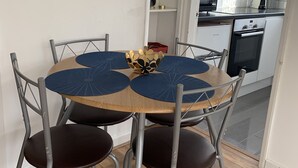 A dining area with a round table, six chairs, and a decorative centerpiece. A kitchen is visible in the background. - London Walthamstow Flat (London)