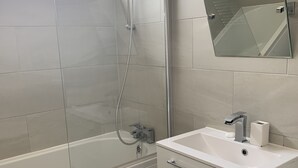 A modern bathroom with a glass-enclosed shower, a white sink with a mirror, and a trash can. - London Walthamstow Flat (London)
