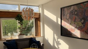 A modern living room with a sofa, a coffee table, and a chair. There is a large window with a view of greenery outside. - London Walthamstow Flat (London)