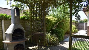 A stone-built outdoor oven, a wooden fence, and a garden area with various plants. - Stoats Old River Way (Winchelsea)