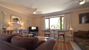 A living room with a sofa, armchairs, a TV, bookshelves, and a window with curtains. - Stoats Old River Way (Winchelsea)