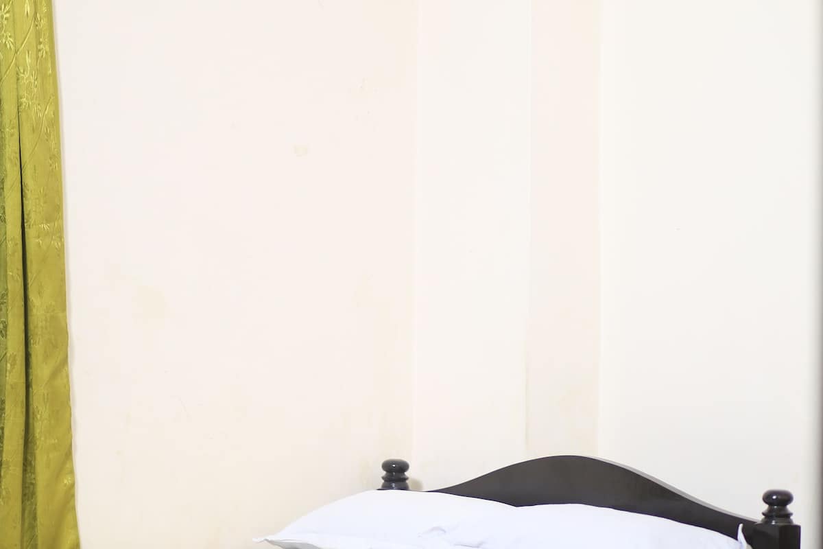 A single bed with a white mattress and a black headboard in a room with a tiled floor.