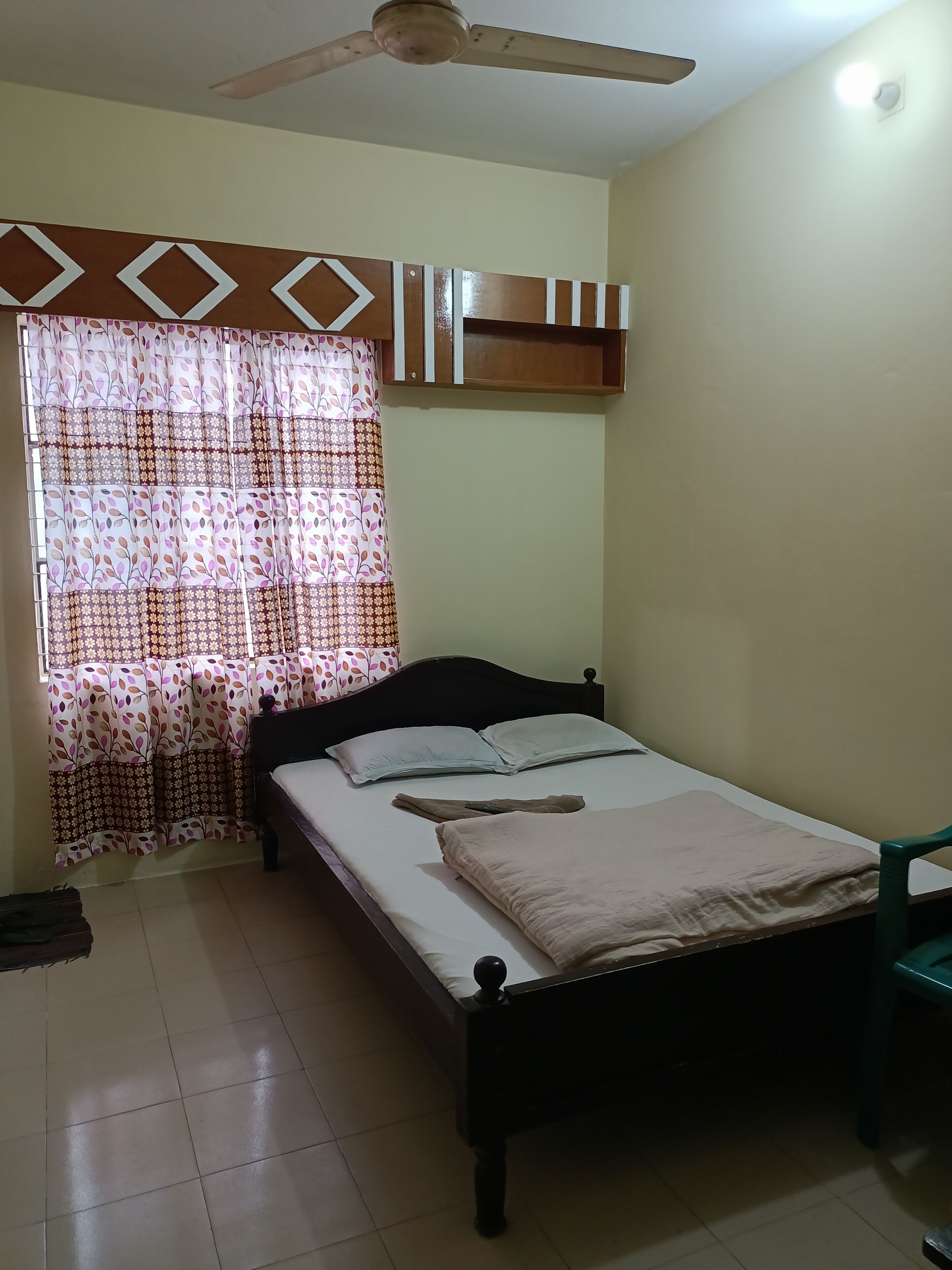 A bedroom with a bed, a ceiling fan, and a window with patterned curtains.