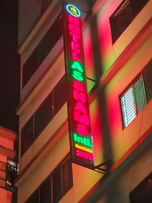 Une enseigne d’hôtel portant le nom « HÔTEL ASHAM » et les mots « Int’l » et « 24 h », indiquant un service international et une disponibilité 24 heures sur 24.