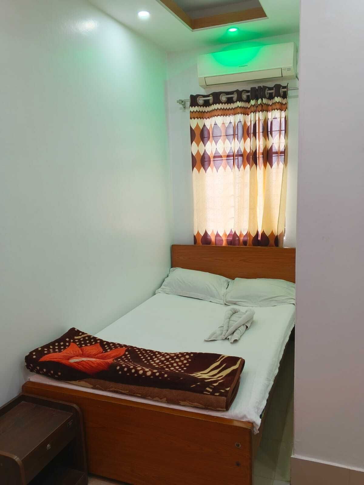 Una habitación pequeña y ordenada con una cama individual, una mesita de noche y una ventana con cortinas estampadas.