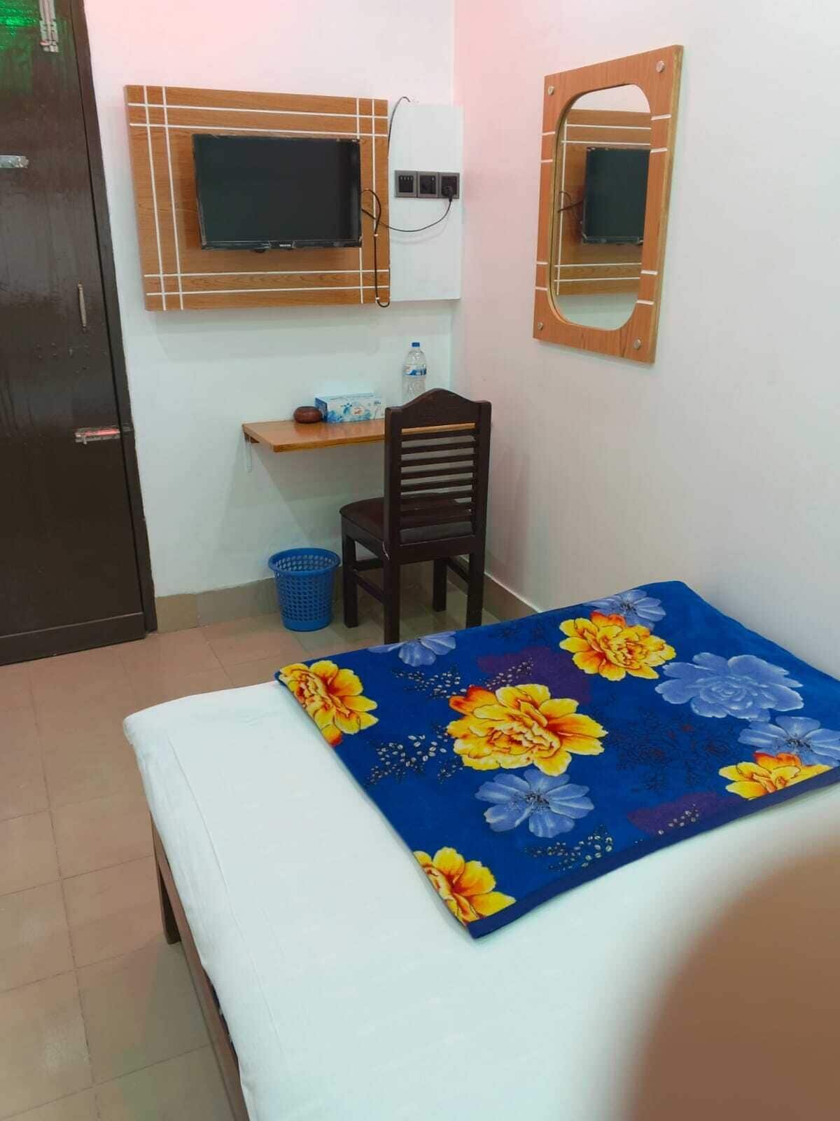 A small room with a bed, a desk, and a chair. There is a television mounted on the wall above the desk.