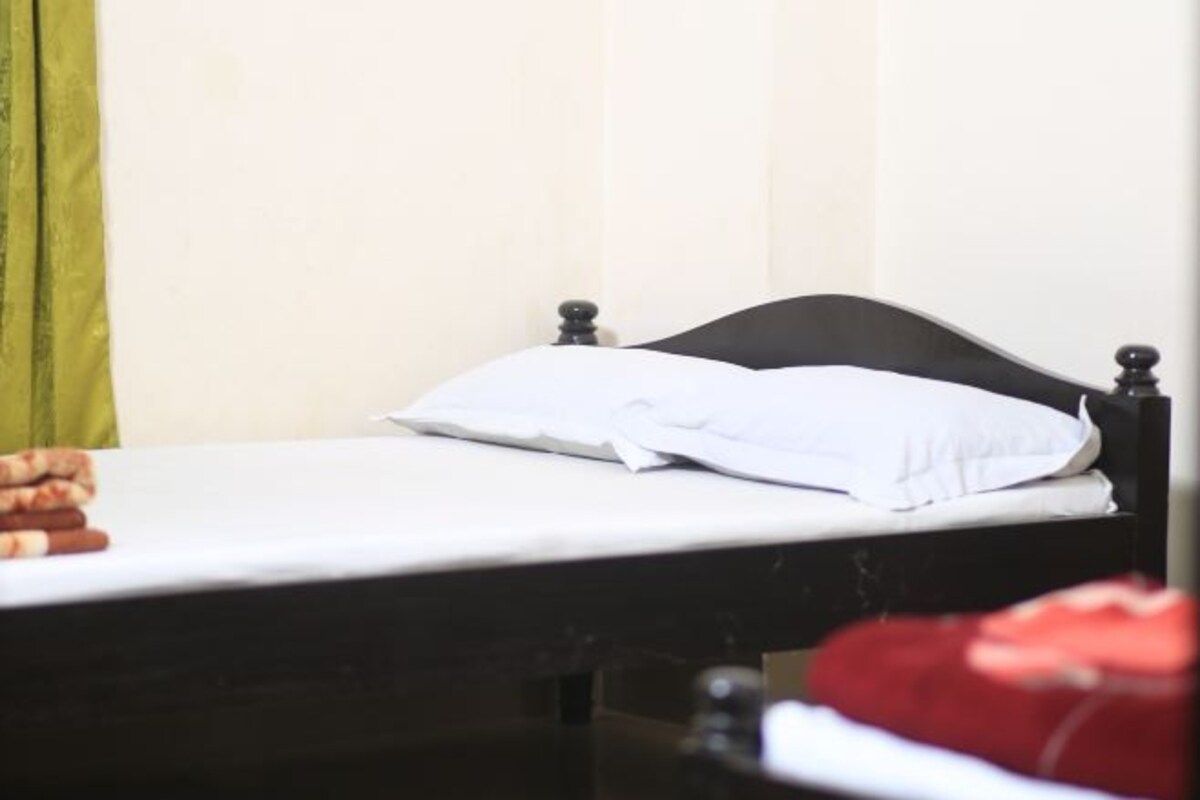 A single bed with a black headboard and white bedding in a room with a plain wall and a green curtain.