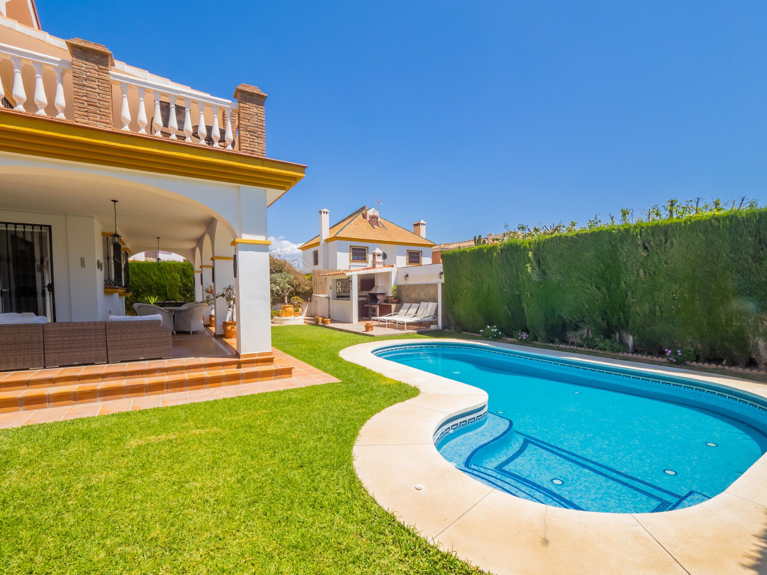 Una casa moderna con piscina, un porche cubierto y un césped cuidado.
