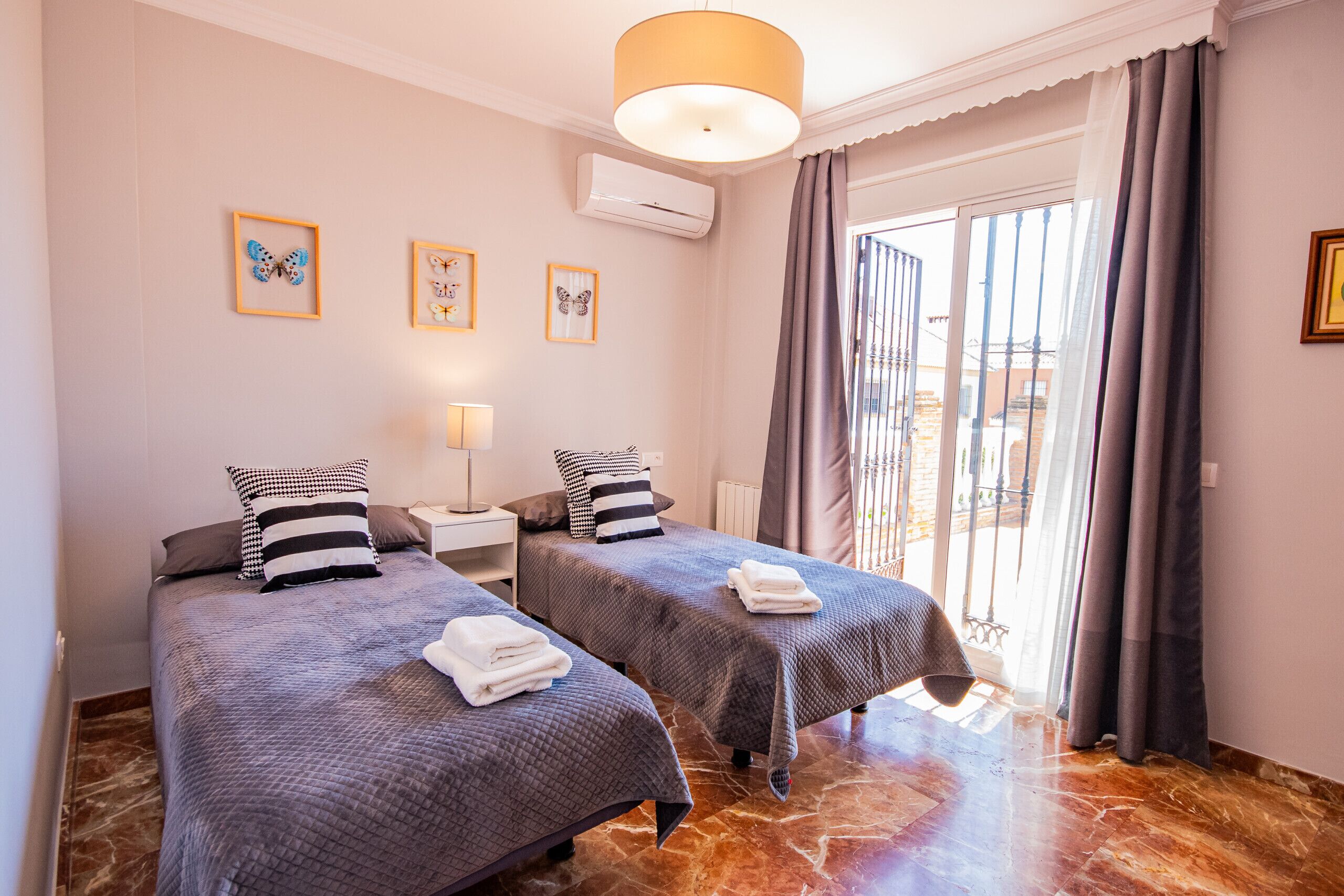 Habitación de hotel con dos camas, una ventana con cortinas, aire acondicionado instalado en la pared y cuadros enmarcados.