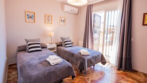 Une chambre d’hôtel avec deux lits, une fenêtre avec des rideaux, un climatiseur fixé au mur et des œuvres d’art encadrées.