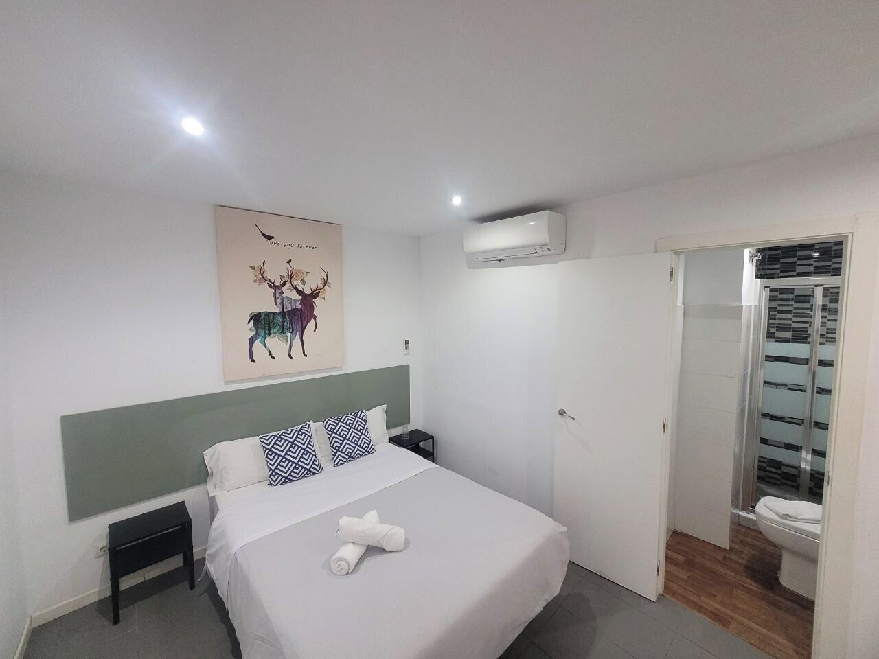 A bedroom with a bed, a nightstand, an air conditioning unit, a bathroom with a toilet and a shower.