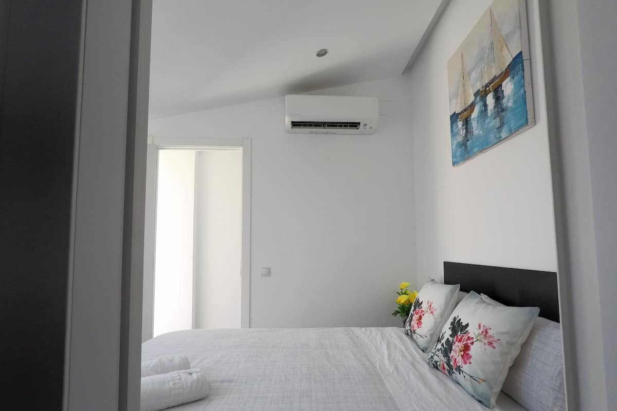 A bedroom with a bed, a wall-mounted air conditioner, and a painting.