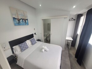 Une chambre d’hôtel bien rangée, avec un lit, une petite table, une chaise et un tableau accroché au mur.