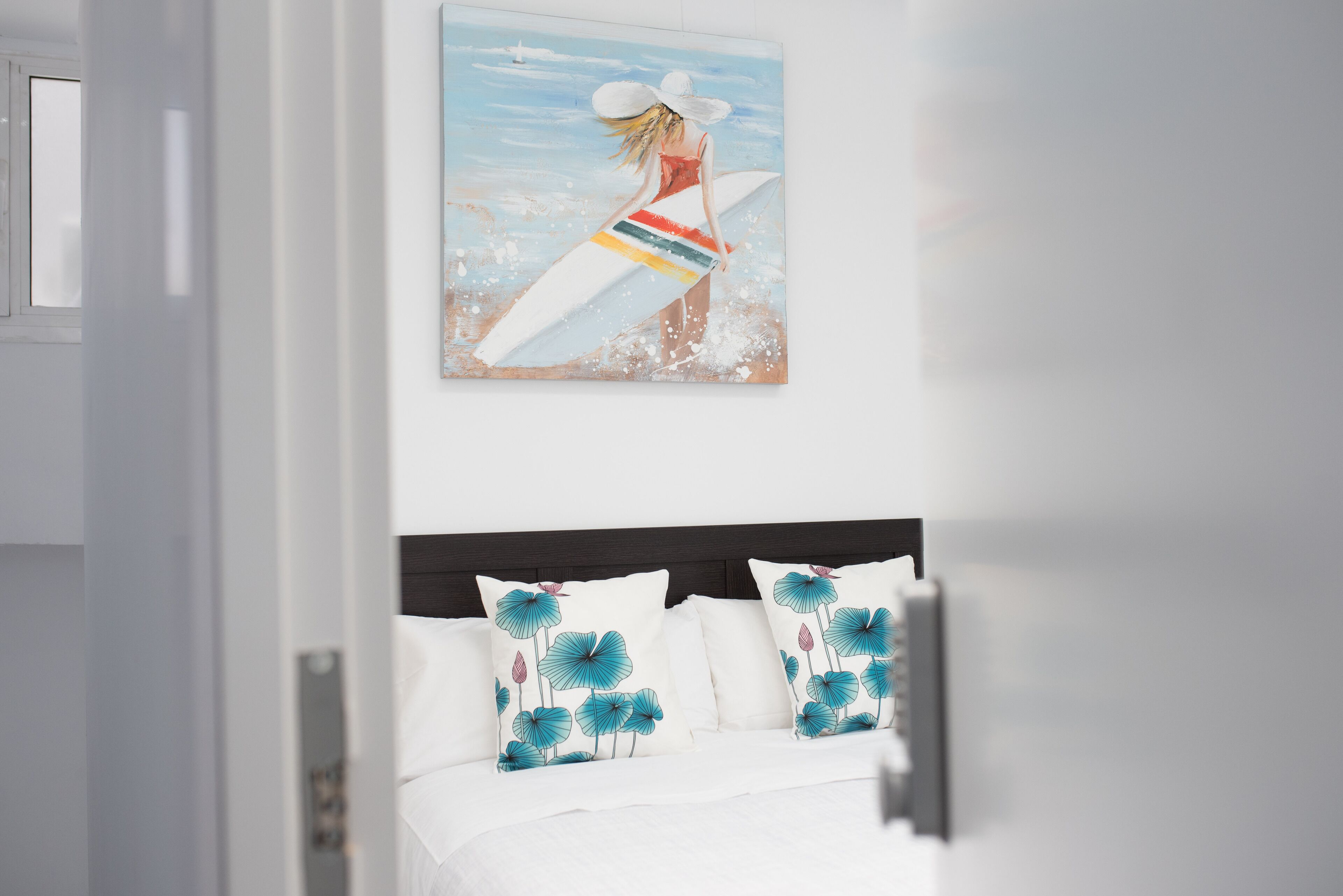 Une chambre à coucher avec un lit, du linge de lit blanc et deux coussins décoratifs aux motifs floraux bleus et roses.