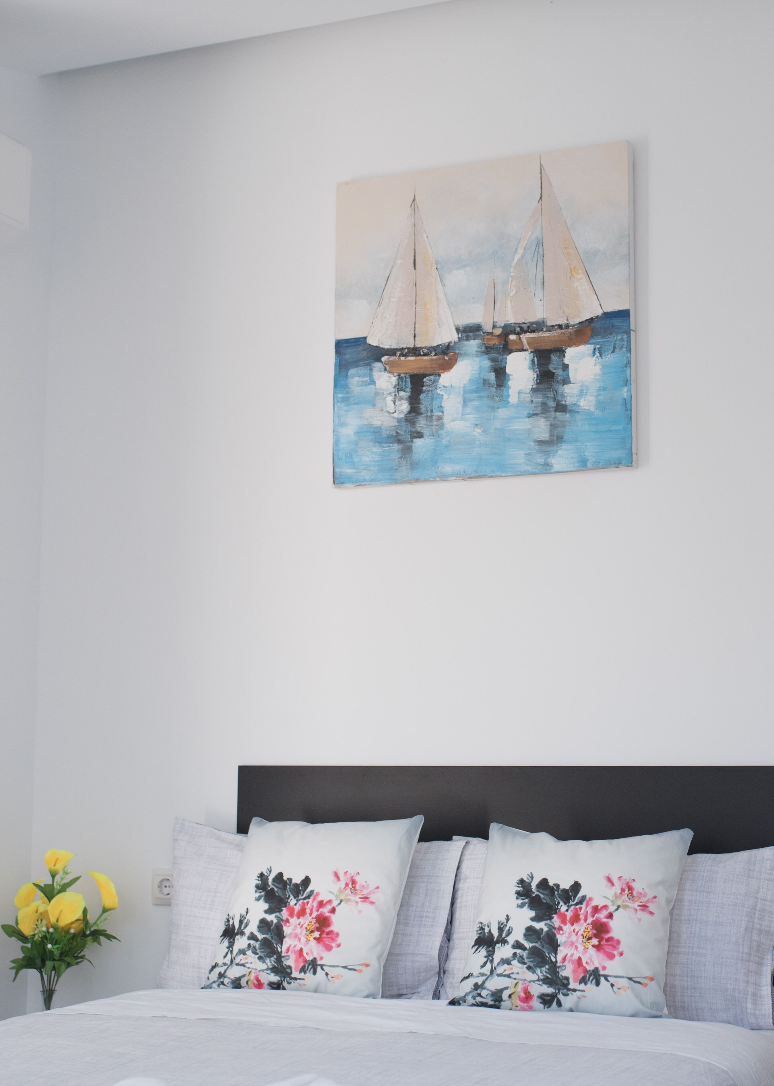 A bedroom with a bed, pillows, and a painting of sailboats on the wall.