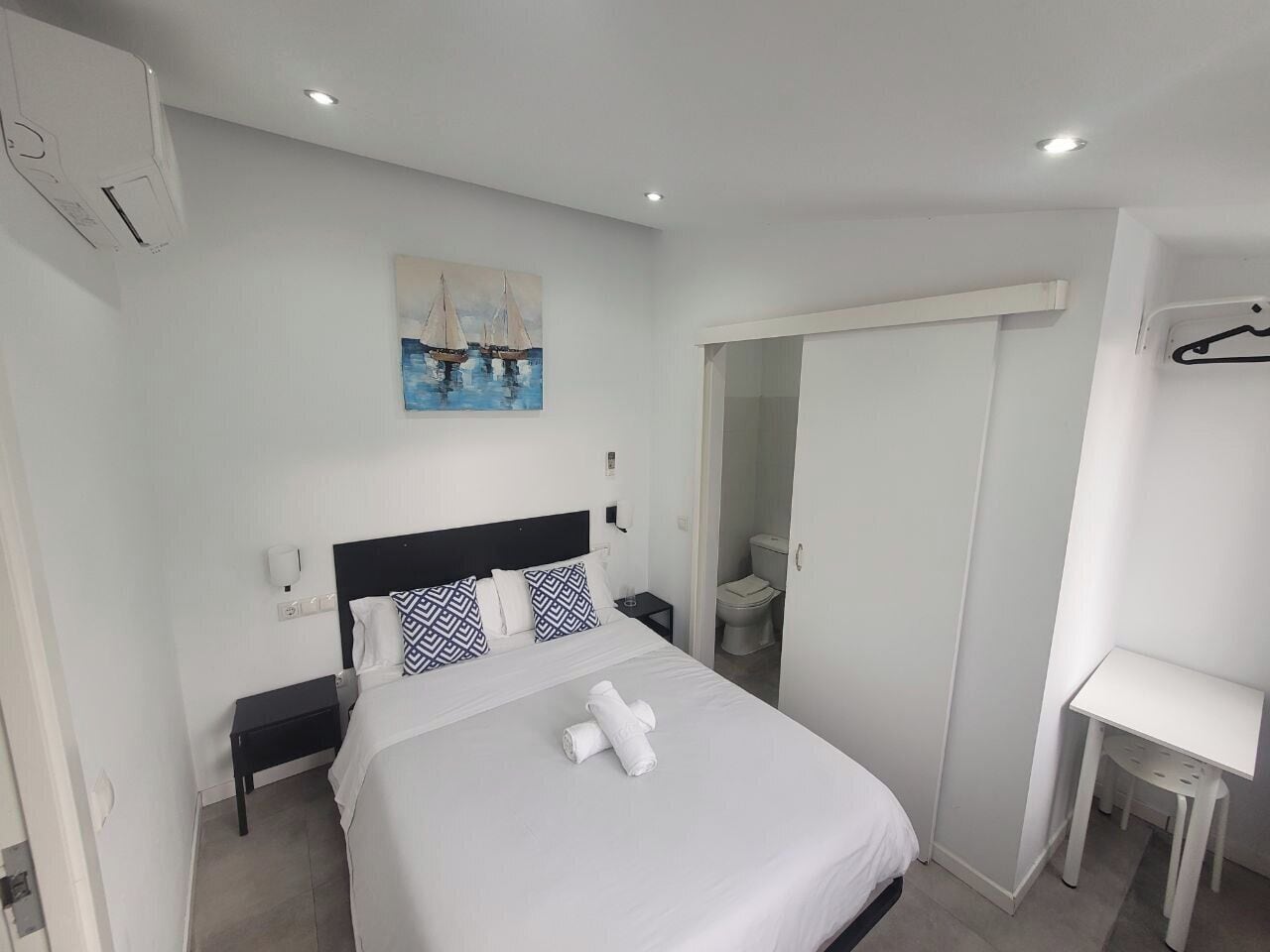 A modern hotel room with a neatly made bed, a small bedside table, a desk, and a wardrobe.