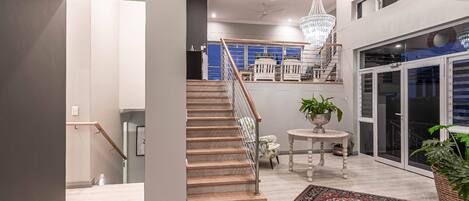 A modern interior with a staircase, a chandelier, and a view of a balcony.