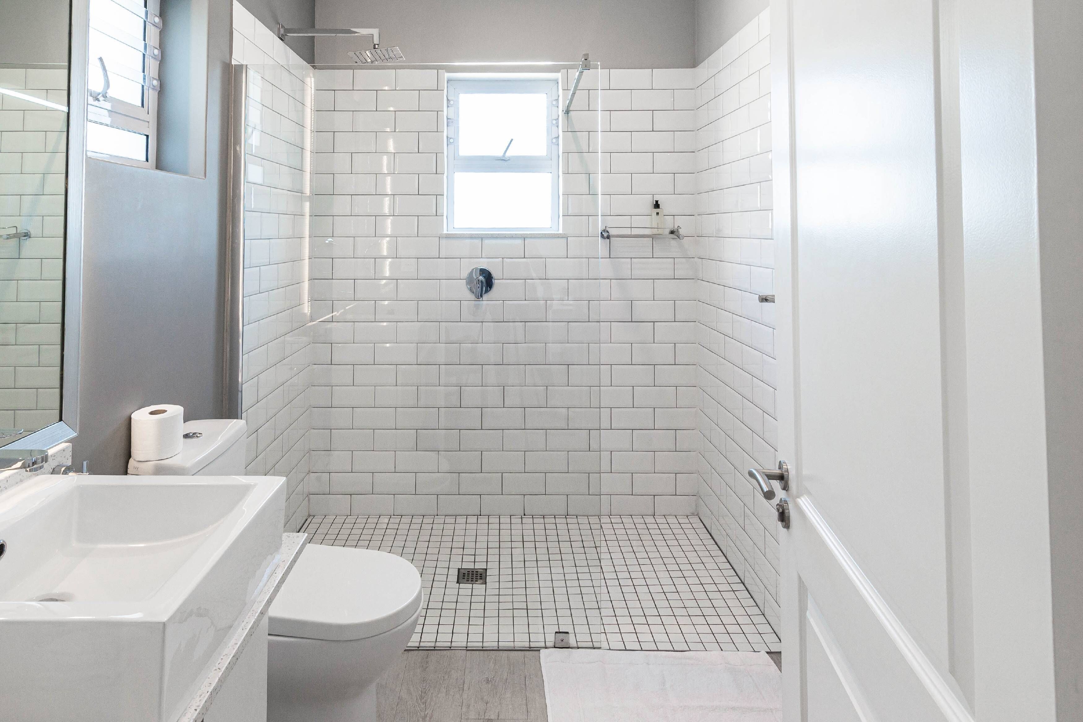 A modern bathroom with white tiles, a bathtub, a toilet, and a shower area.