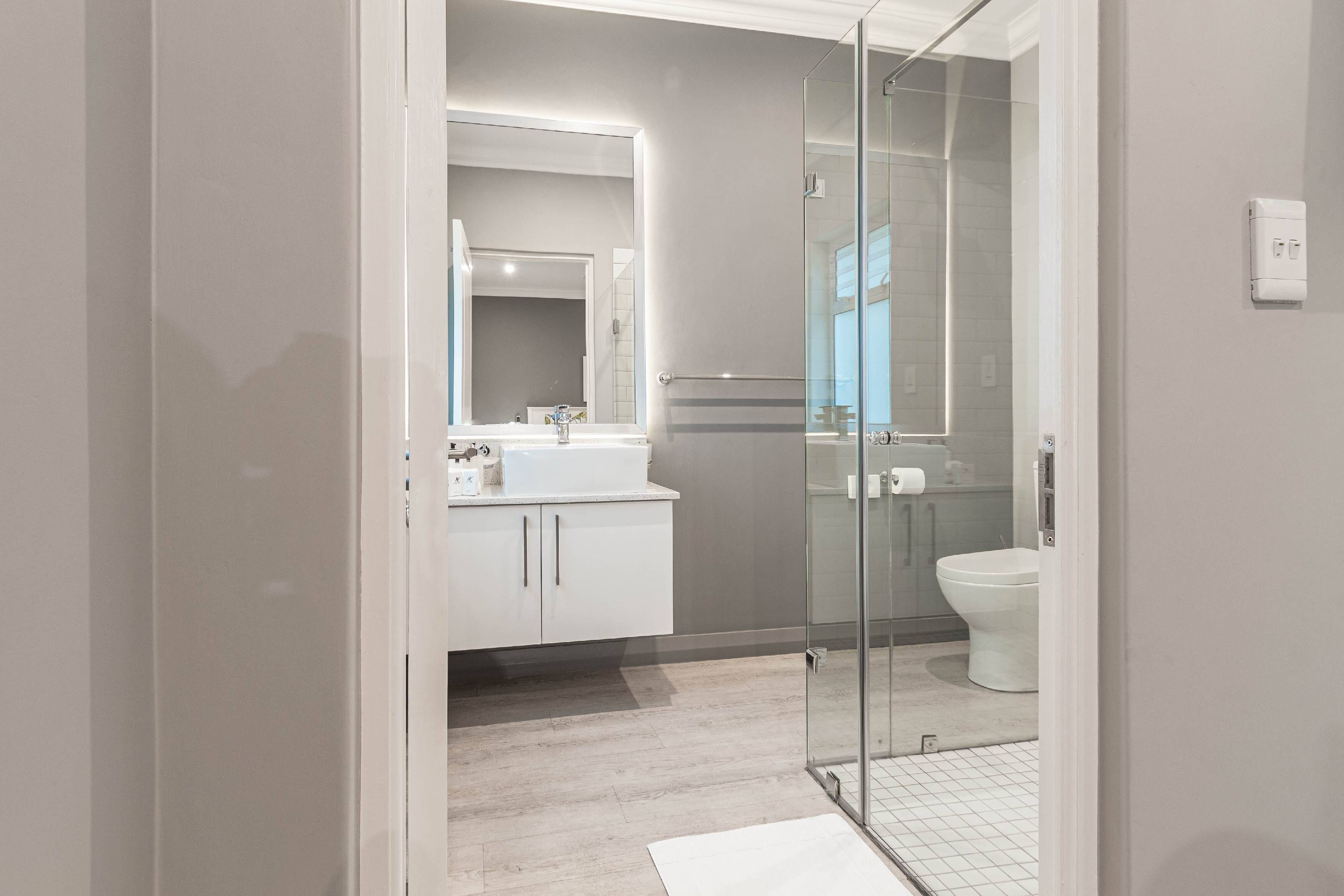 Un baño moderno con cabina de ducha de vidrio, un lavabo blanco y un inodoro.