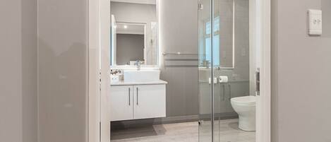 Un baño moderno con cabina de ducha de vidrio, un lavabo blanco y un inodoro.