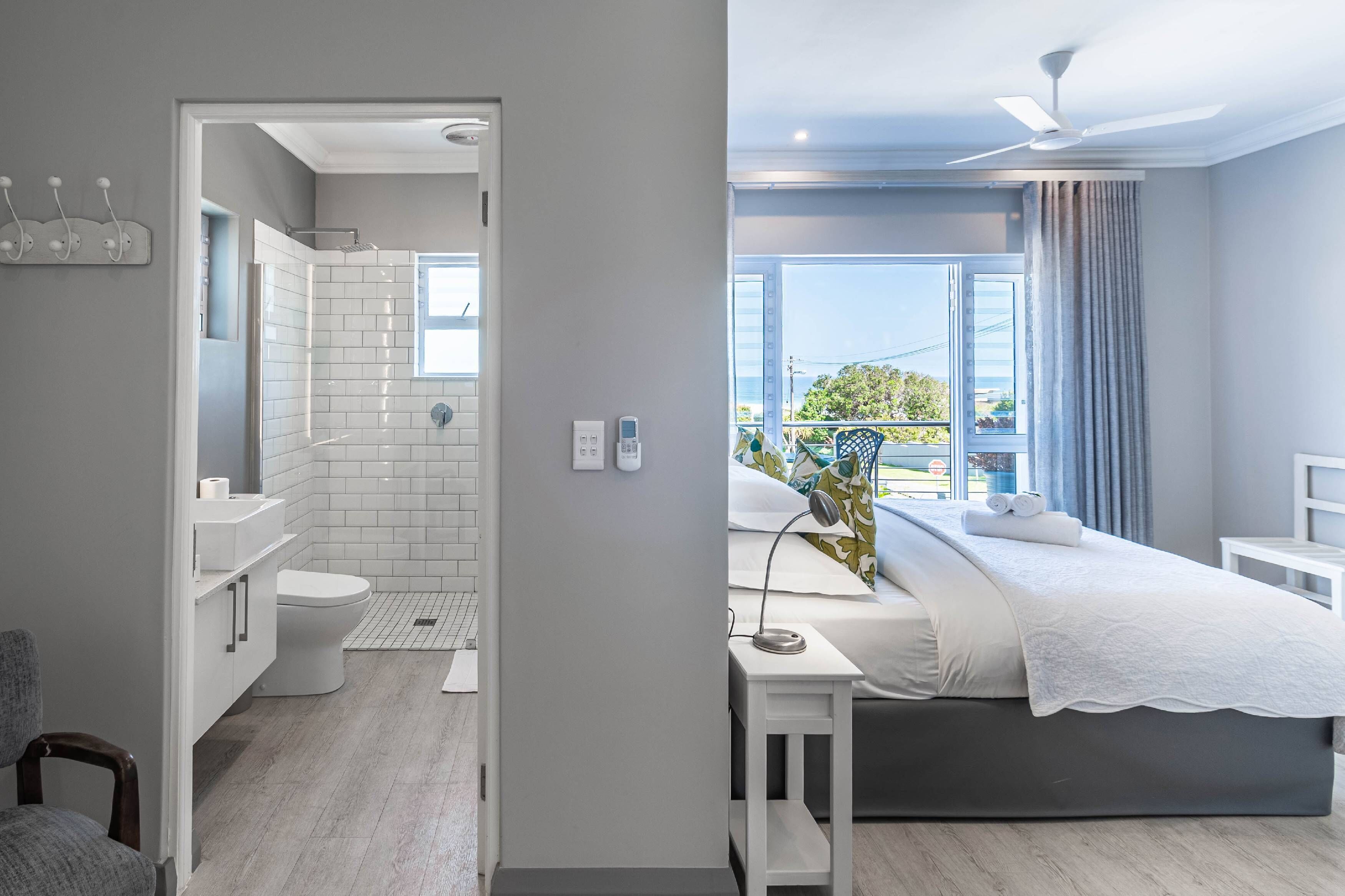 Un baño moderno con ducha, inodoro y lavamanos. Se ve una cama con vistas al exterior.