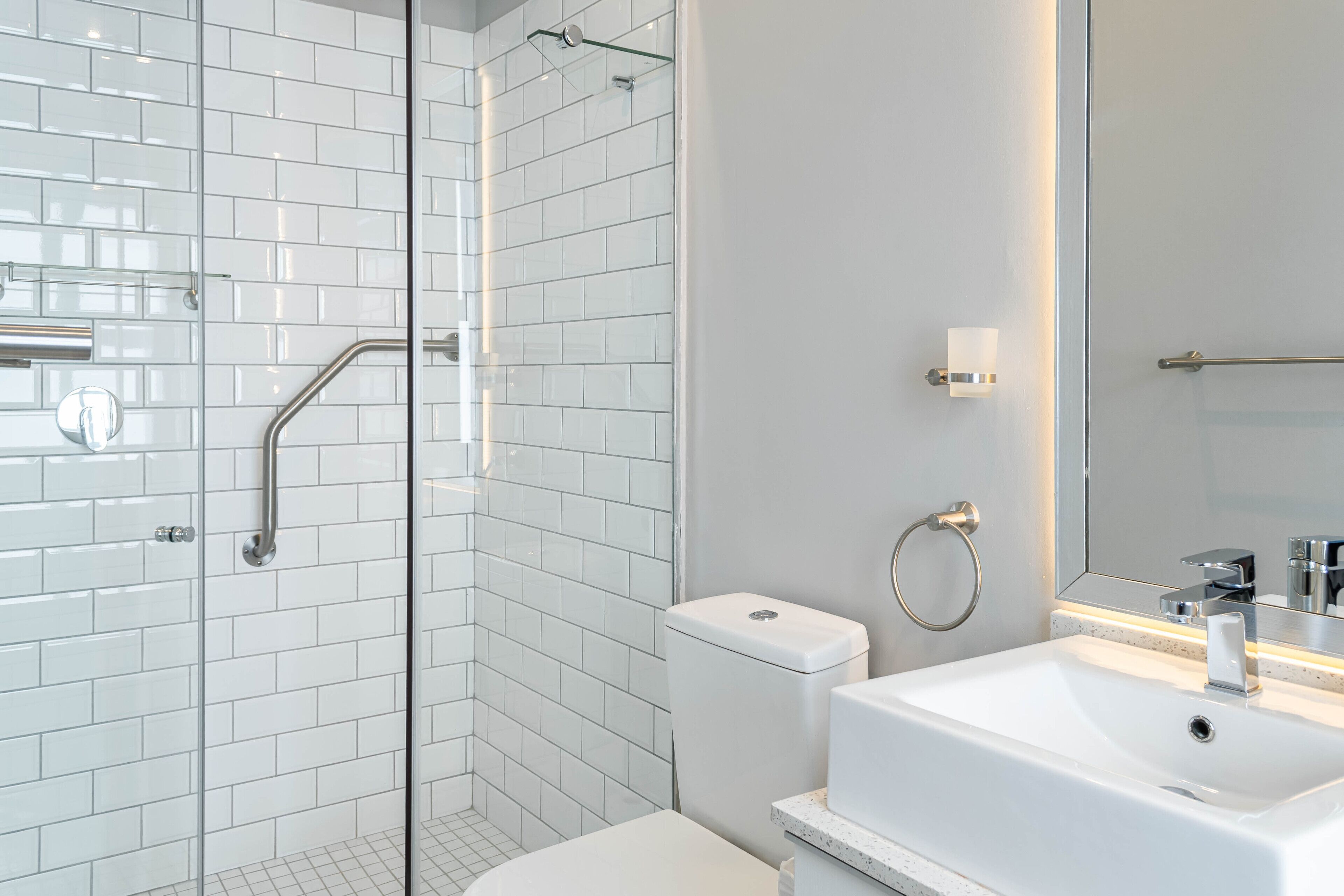 A modern bathroom with white subway tiles, a glass shower enclosure, a white toilet, and a sink with a mirror.
