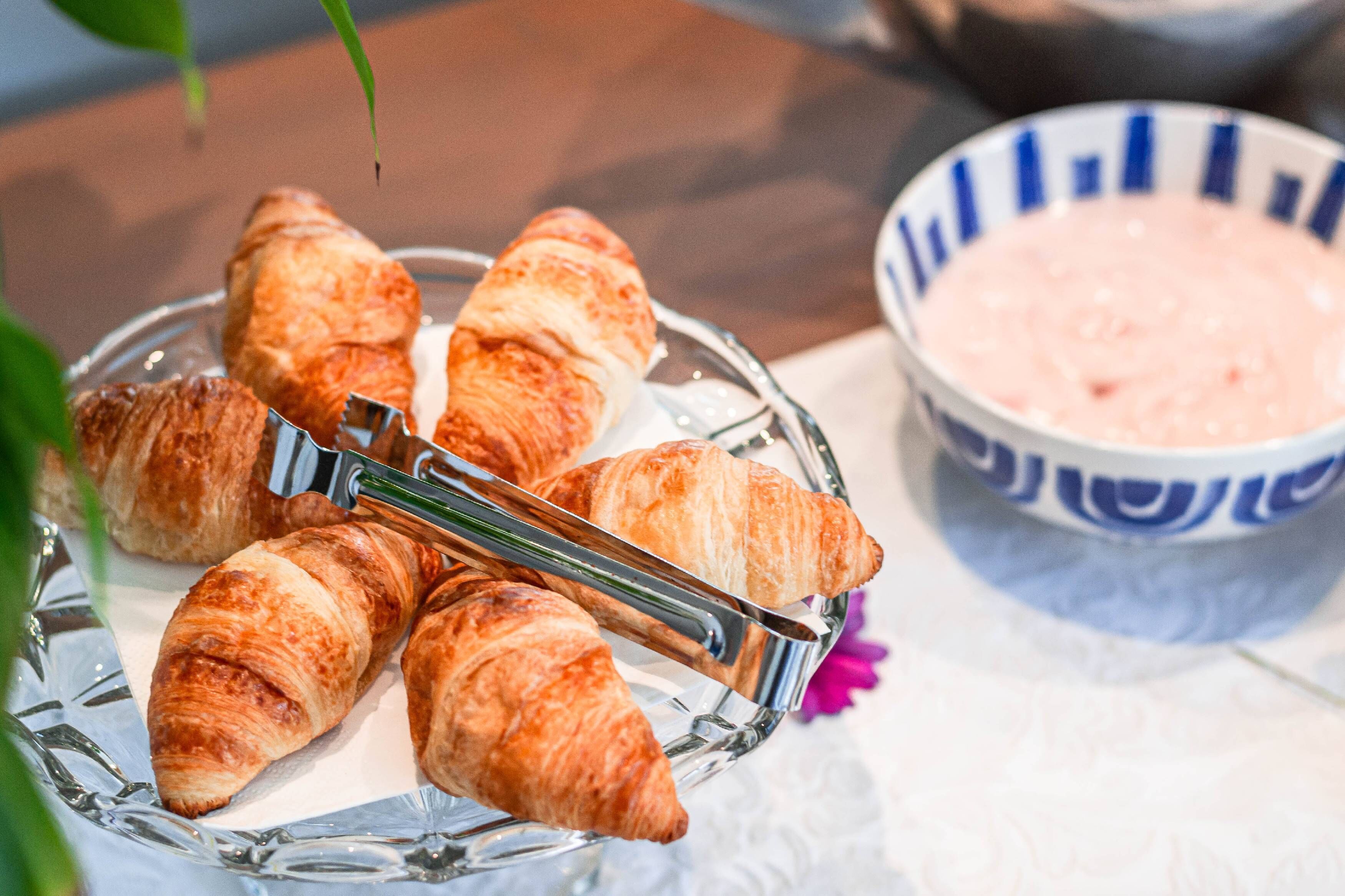 A glass plate with croissants and a bowl of pink dip.