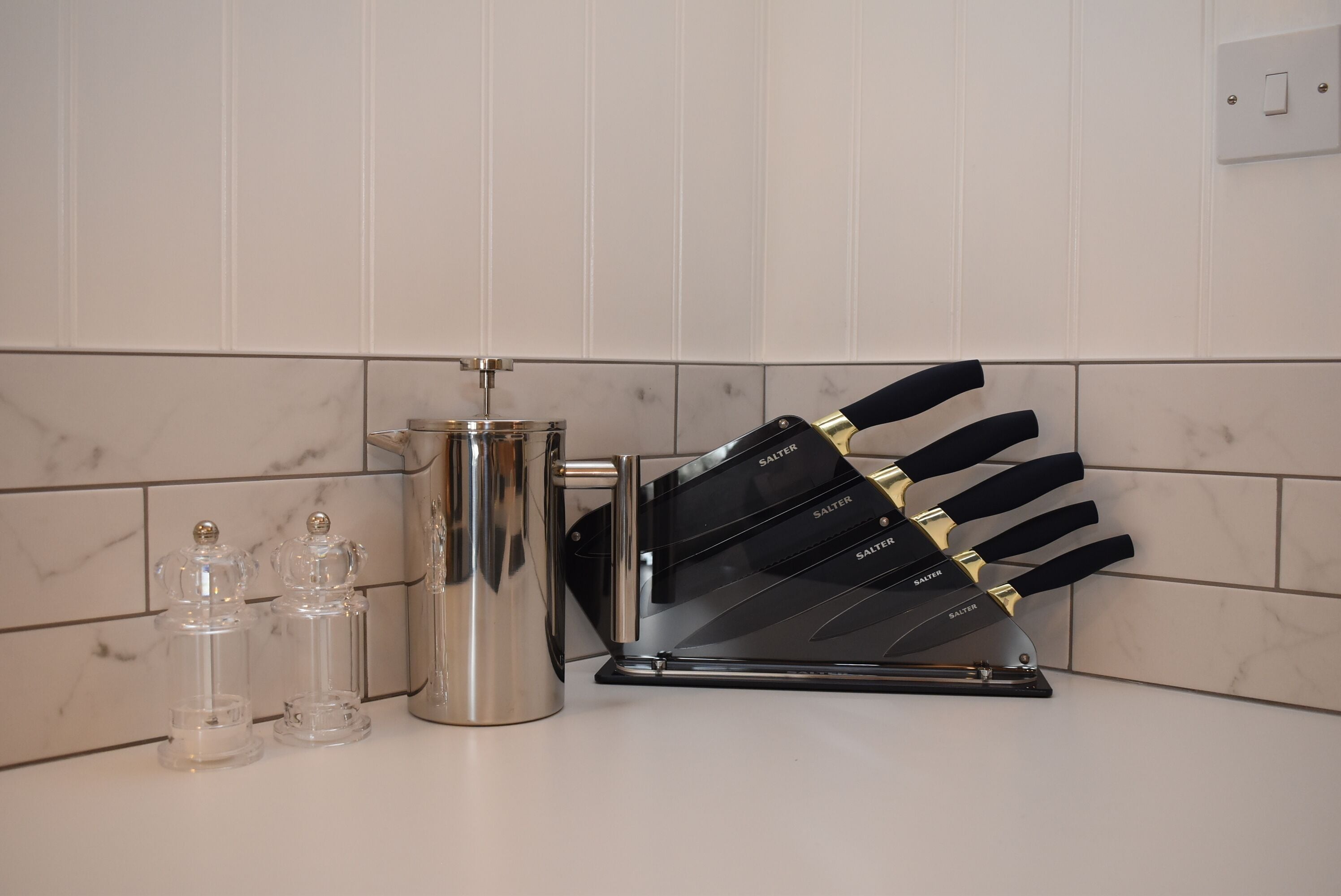 Un piano di lavoro in cucina con un bollitore in acciaio inossidabile, un portacoltelli e due saliera.