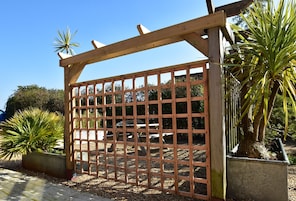 Um portão de madeira com design em grade, rodeado por vasos de plantas e um céu claro.