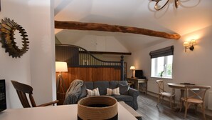 A cozy living room with a staircase, a dining area, and a large woven basket on a table. - Buttercup Cottage (Rye)