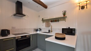 A modern kitchen with a built-in oven, microwave, and a coffee maker on the counter. - Buttercup Cottage (Rye)