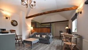 A cozy living room with a grey sofa, wooden chairs, a small table, and a staircase leading to another room. - Buttercup Cottage (Rye)