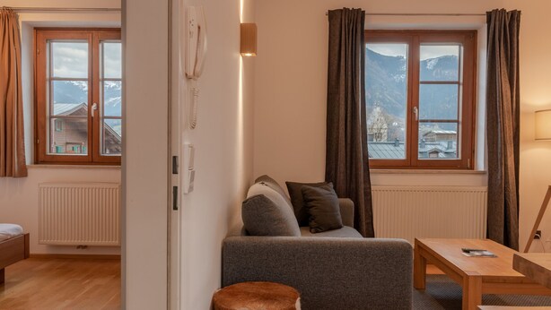 Ein gemütliches Zimmer mit einer Couch, einem Holztisch und Blick auf Berge durch die Fenster.