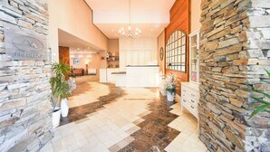A hotel lobby with a stone wall, a chandelier, a reception desk, and a kitchen area. - Predela LUX (Bansko)