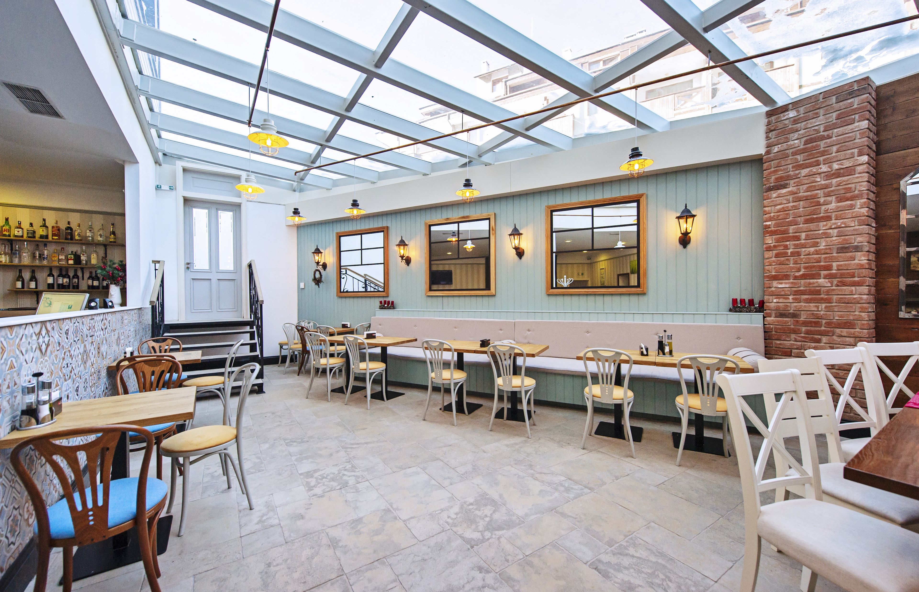 A restaurant with a high ceiling and skylight, wooden tables and chairs, and a brick wall.