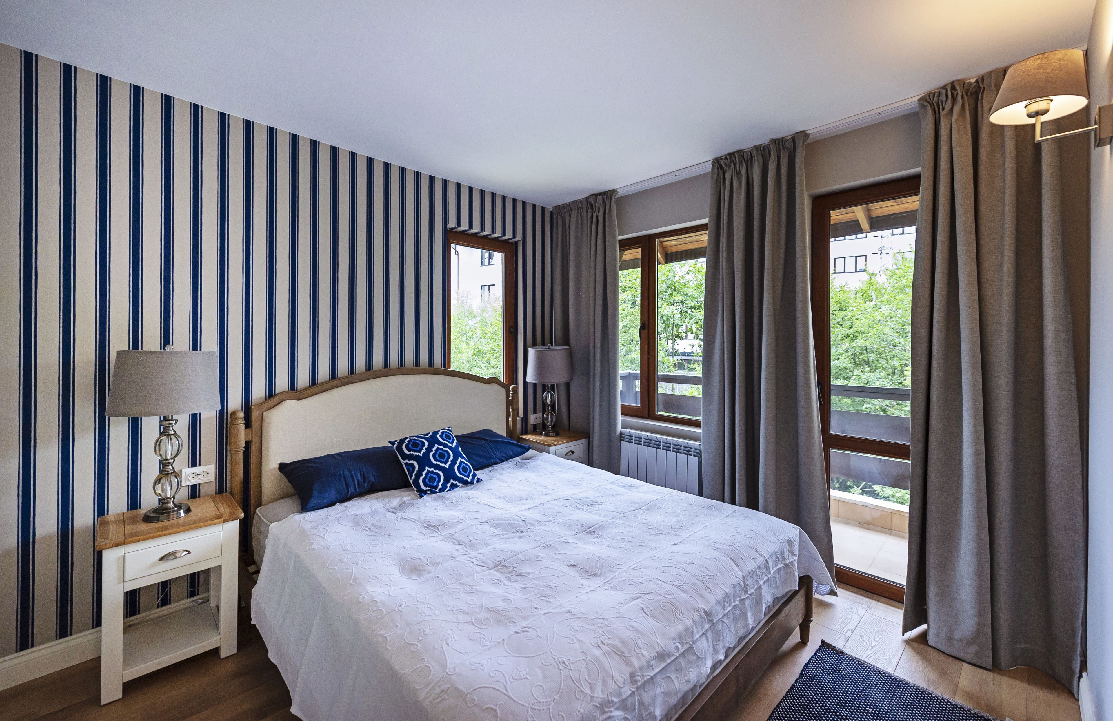 A hotel room with a large bed, striped wallpaper, and a view of greenery outside.