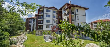 A multi-story residential building with balconies, a stone pathway, and a grassy lawn.