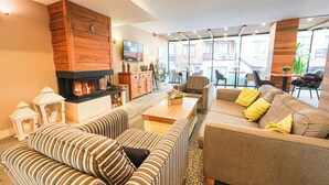 A modern living room with a fireplace, striped sofas, and a large window offering a view of the outside. - Predela LUX (Bansko)