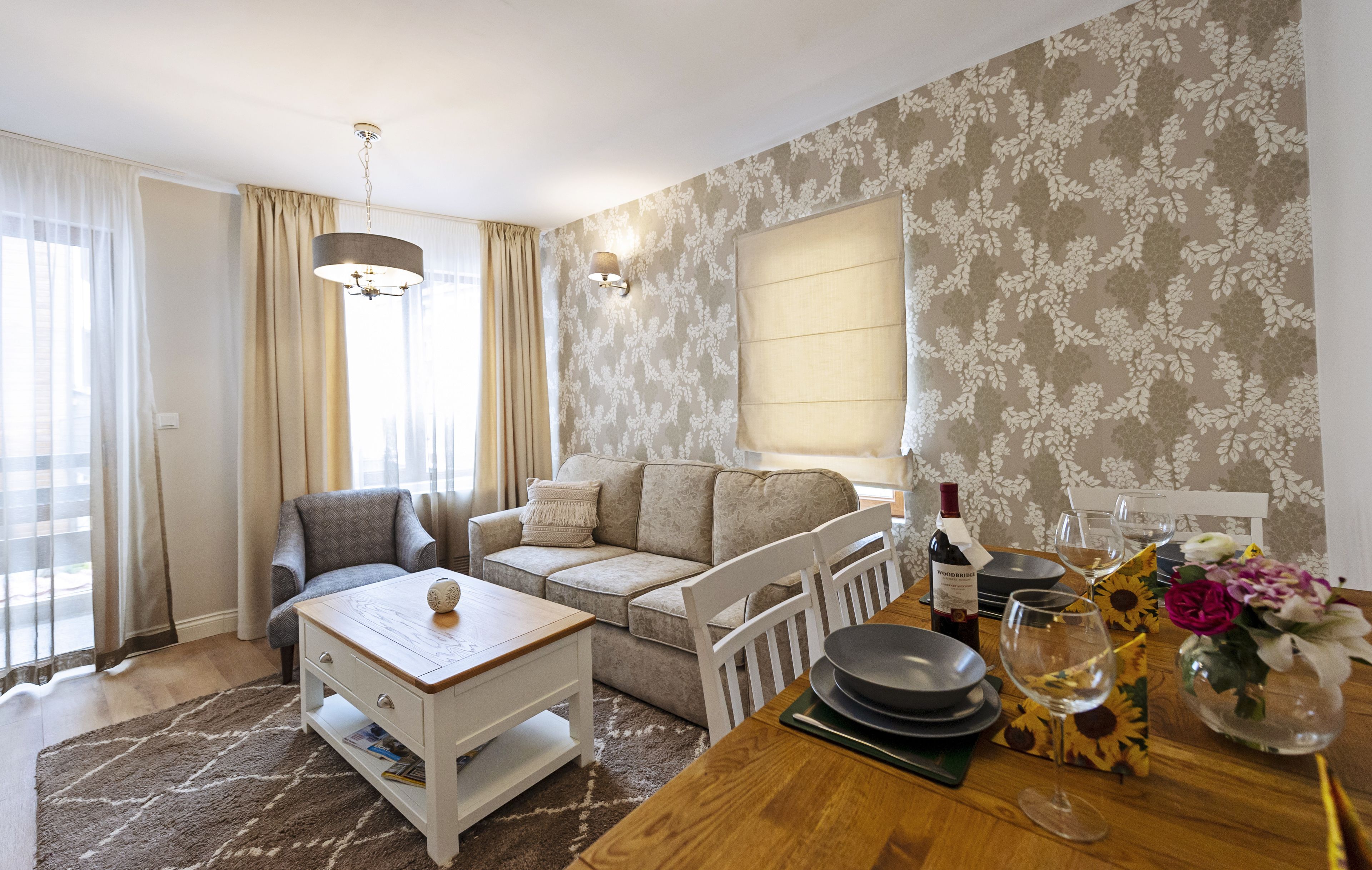 A modern living room with a sofa, a coffee table, and a dining area set with plates, glasses, and a bottle.