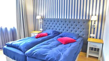 A double bed with blue bedding and red pillows, two bedside tables with lamps, and a striped wall.