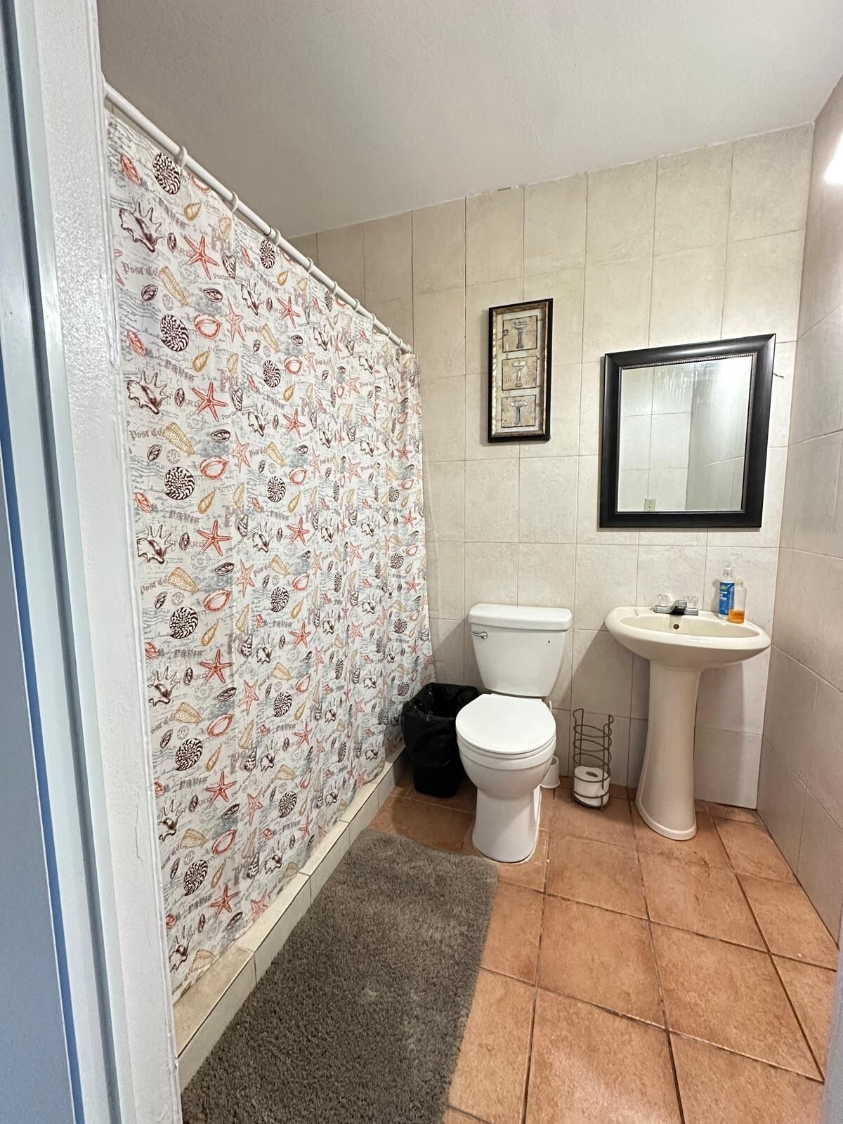 A bathroom with a tiled floor, a toilet, a sink, and a shower curtain with a sea-themed pattern.