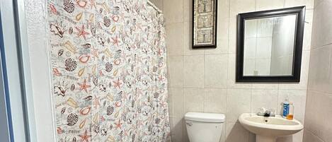 A bathroom with a tiled floor, a toilet, a sink, and a shower curtain with a sea-themed pattern.