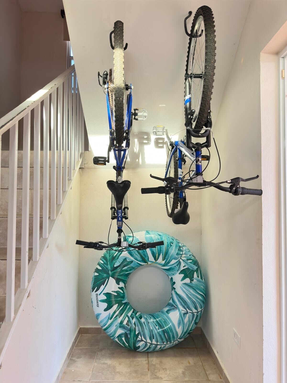 Een trap met twee fietsen aan de muur, een opblaasbare ring in blauw en wit, en een witte leuning.