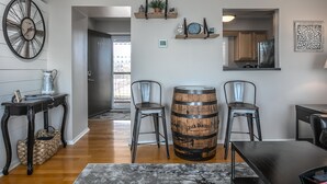 A modern living room with a wooden barrel, two chairs, a coffee table, a clock, and a small plant on shelves.