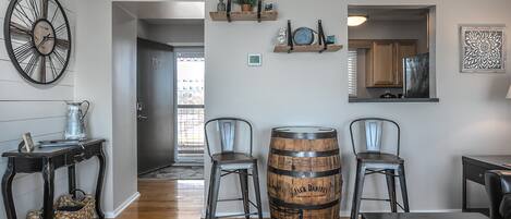 A modern living room with a wooden barrel, two chairs, a coffee table, a clock, and a small plant on shelves.