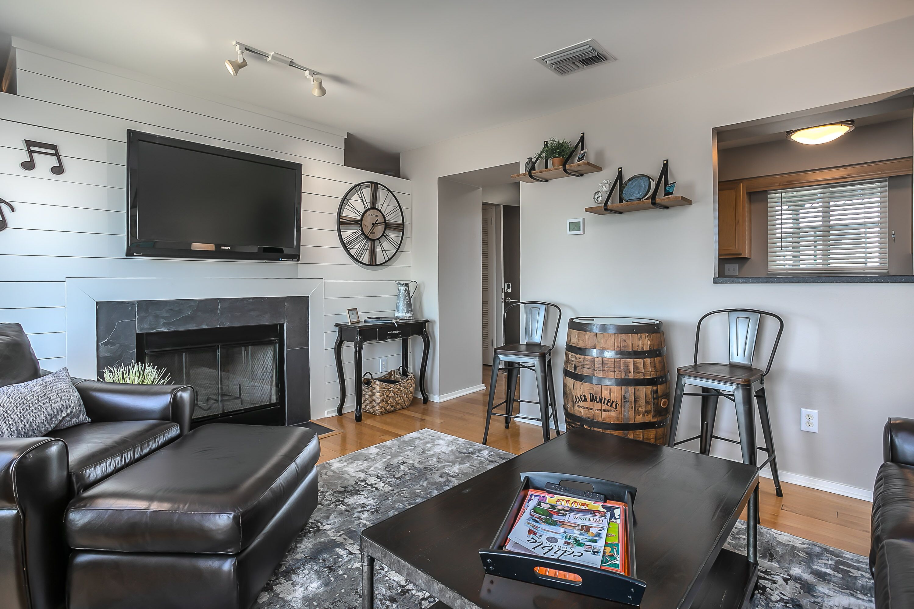 A modern living room with a fireplace, leather furniture, a flat-screen TV, and a bookshelf.