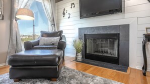 A modern living room with a leather sofa, a fireplace, and a large flat-screen TV mounted on the wall.