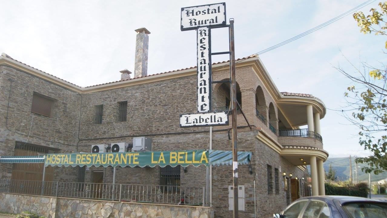 Een landelijk gebouw met een bord waarop staat: "Hostal Rural Restaurante La Bella".