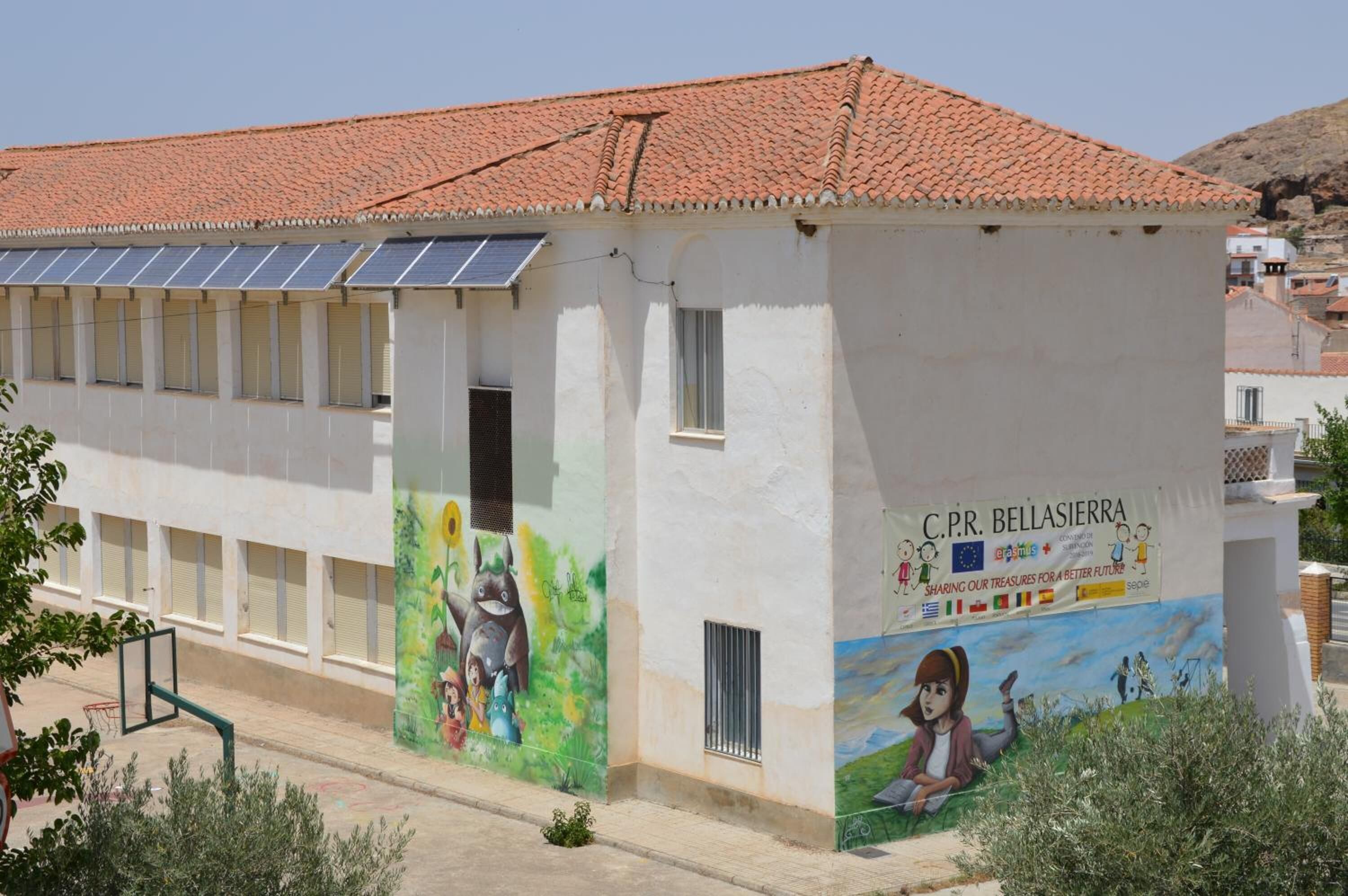 A building with a white facade, red-tiled roof, and solar panels on the roof.